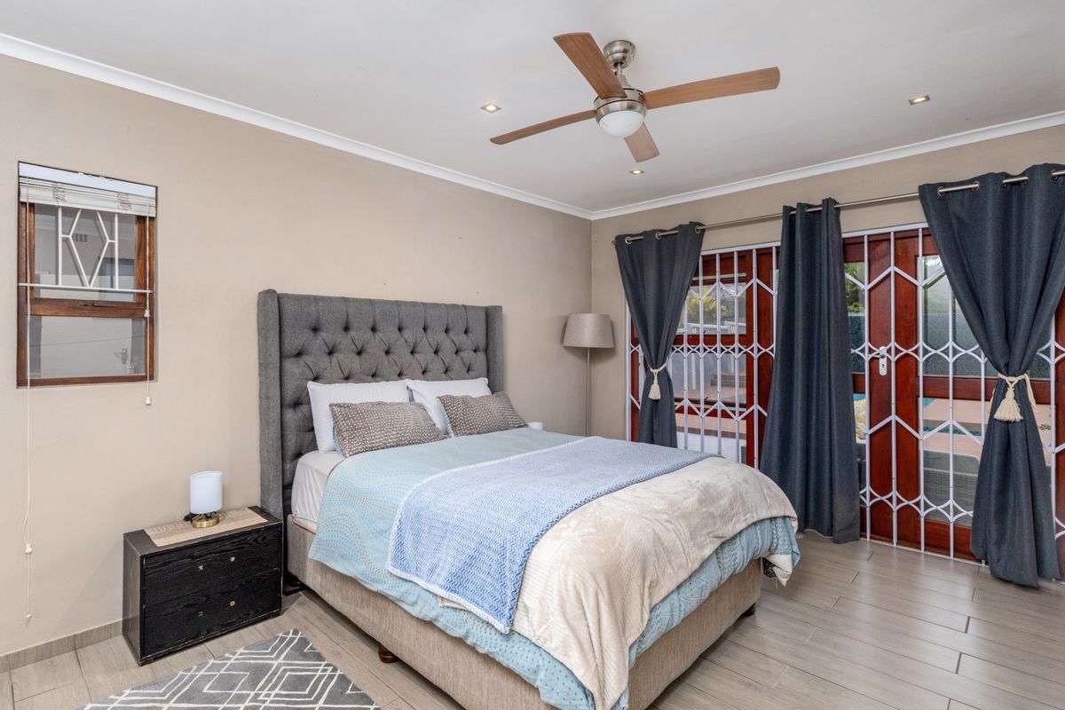 A well-maintained bedroom featuring tiled flooring, a ceiling fan, and direct access to the outdoor area through sliding doors with security gates.