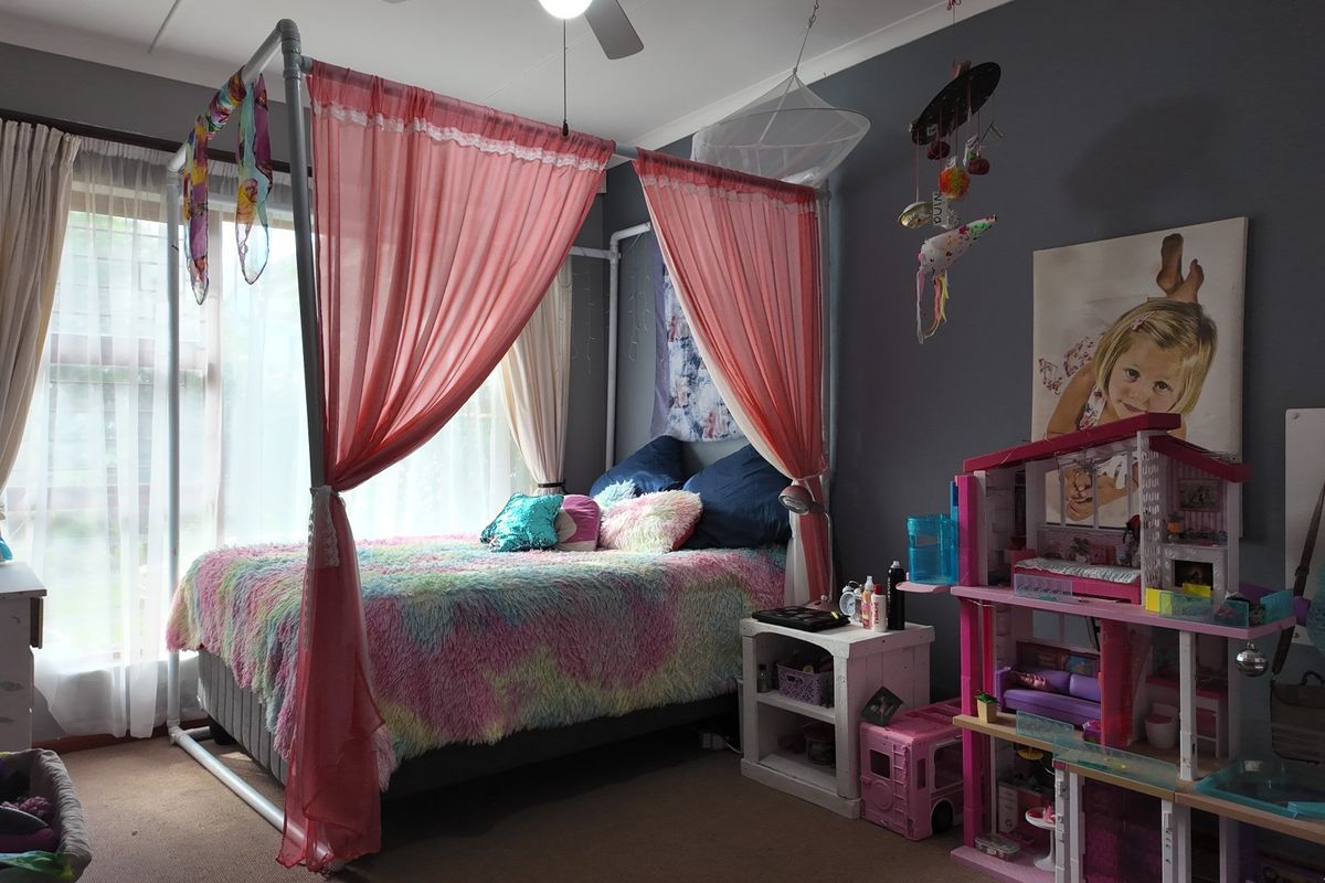 A bedroom featuring a ceiling fan and large window with curtain tracks, currently decorated as a child's room.