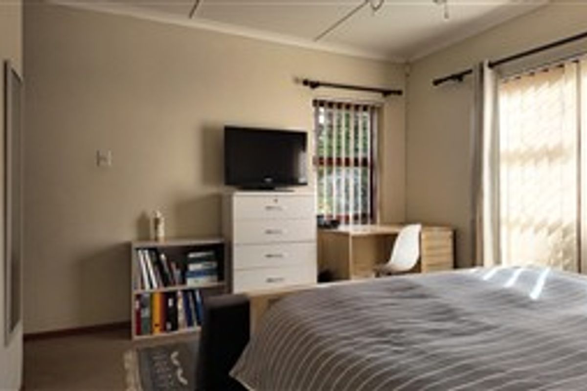 A bedroom featuring neutral walls, carpeted flooring, and a large sliding door with vertical blinds providing natural light.