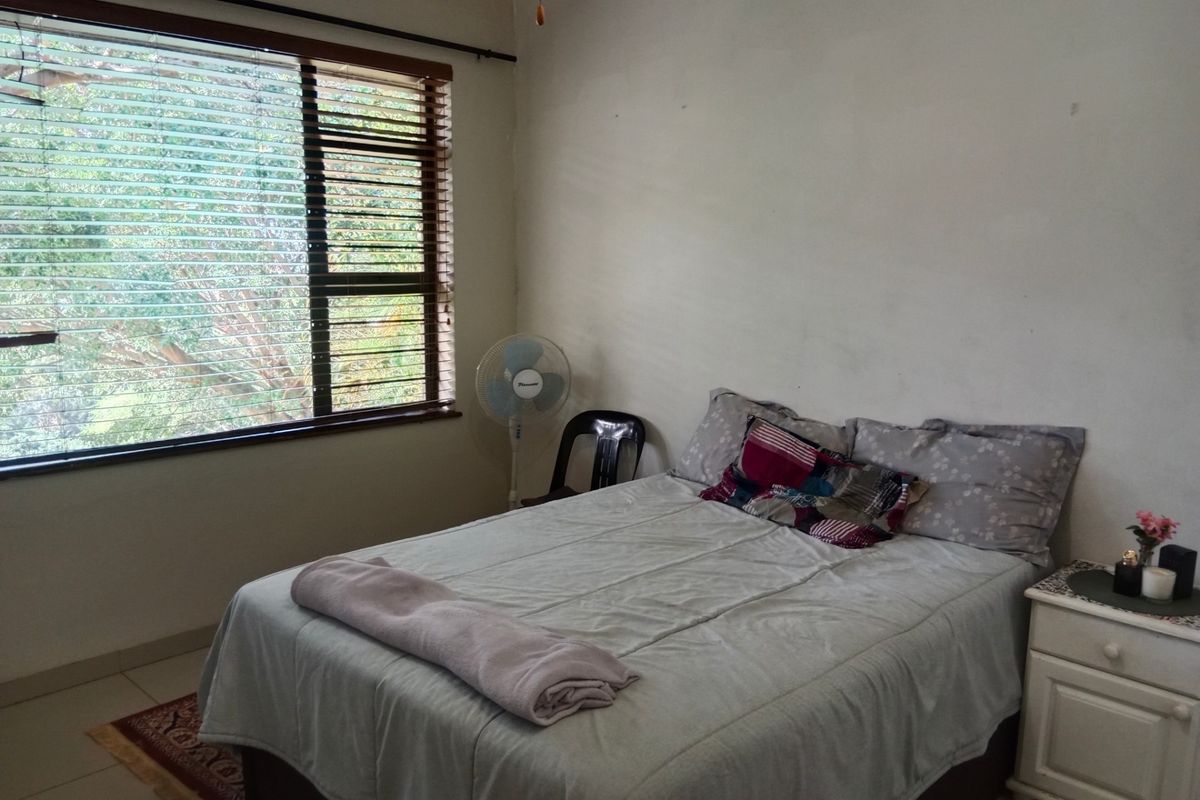 A bedroom featuring tiled flooring, a large window with fitted blinds, and neutral wall finishes.