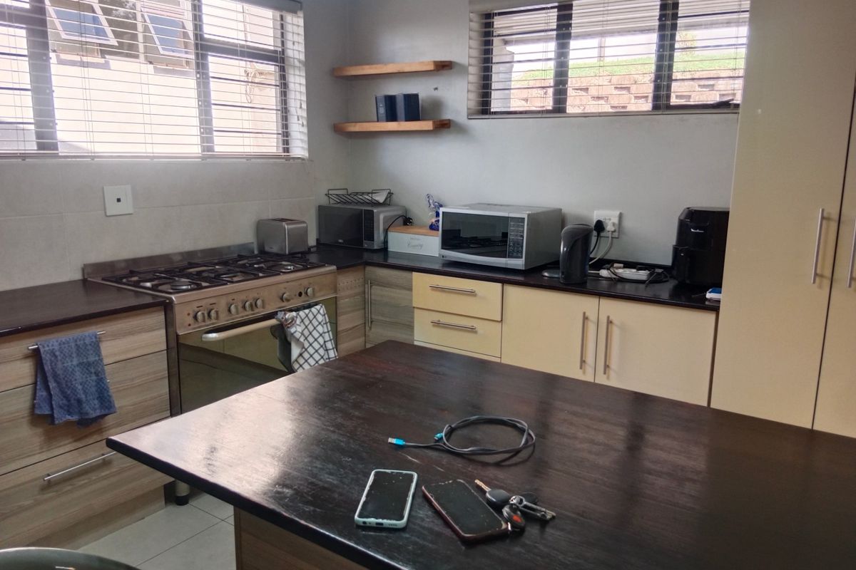 A functional kitchen featuring built-in cabinetry, a gas stove with oven, dark countertops, and a central island, complemented by natural light from windows.