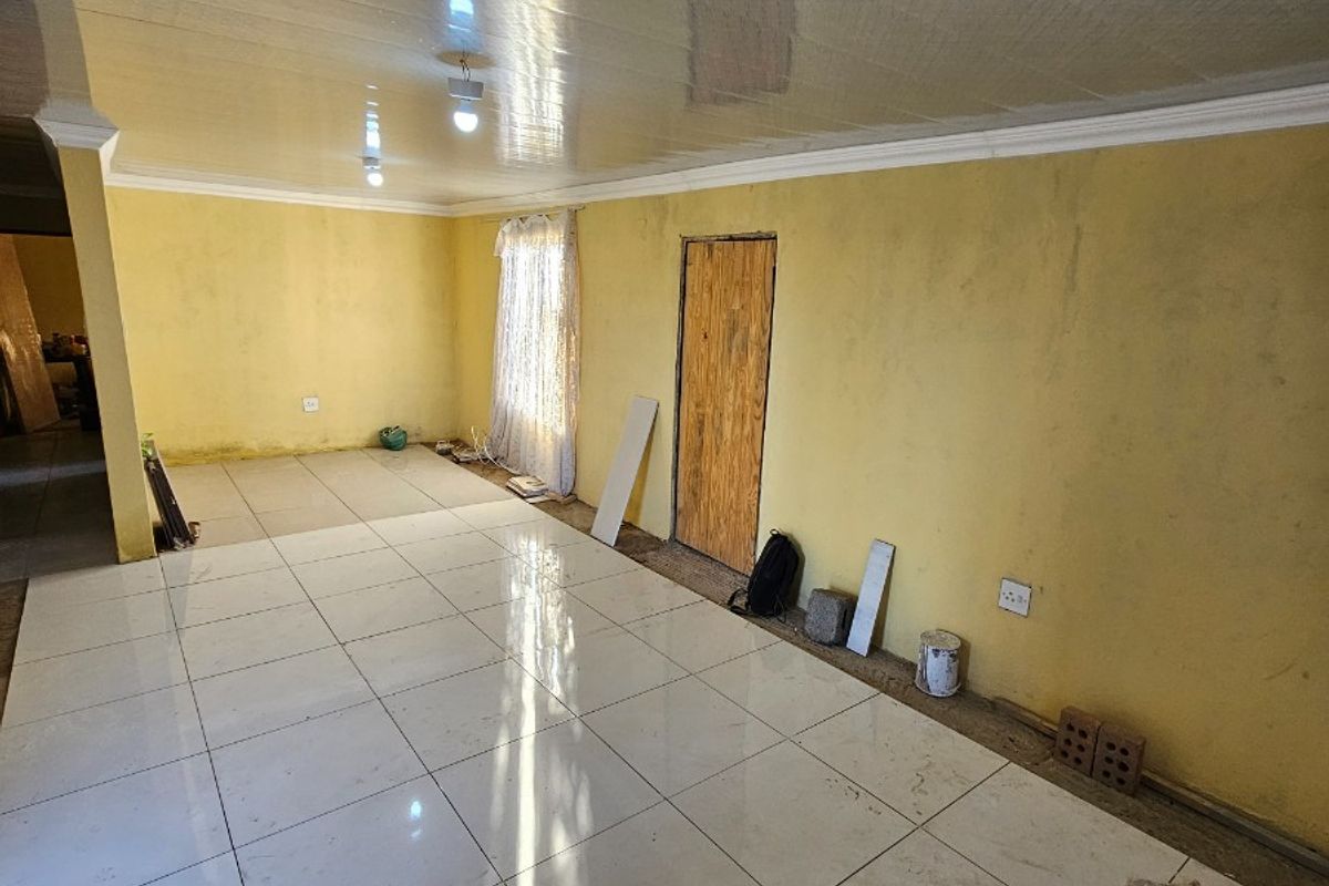 An empty living area featuring large format white floor tiles, yellow painted walls, and a glossy panelled ceiling with integrated lighting.
