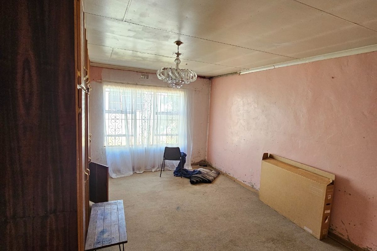 A vacant bedroom featuring built-in wooden cabinetry, a central light fixture, and a window with security bars, requiring cosmetic updates and flooring replacement.