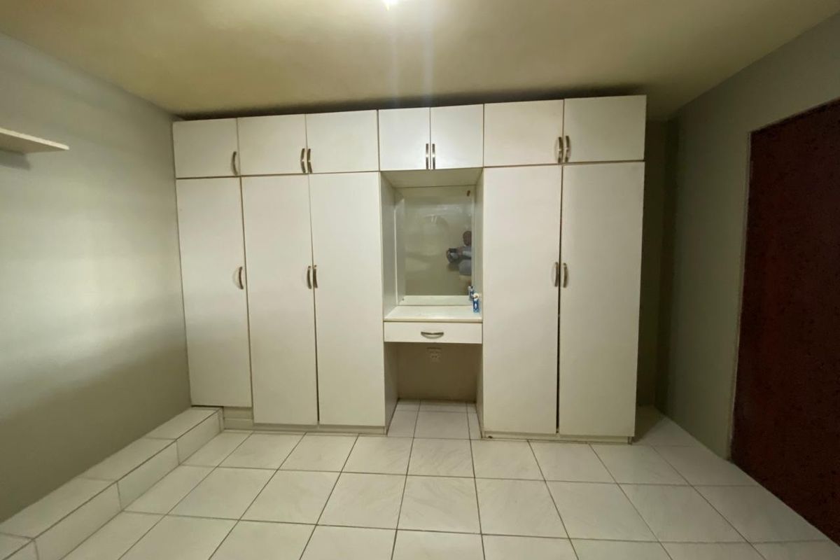 A bedroom featuring built-in white cabinetry with an integrated vanity mirror and tiled flooring.