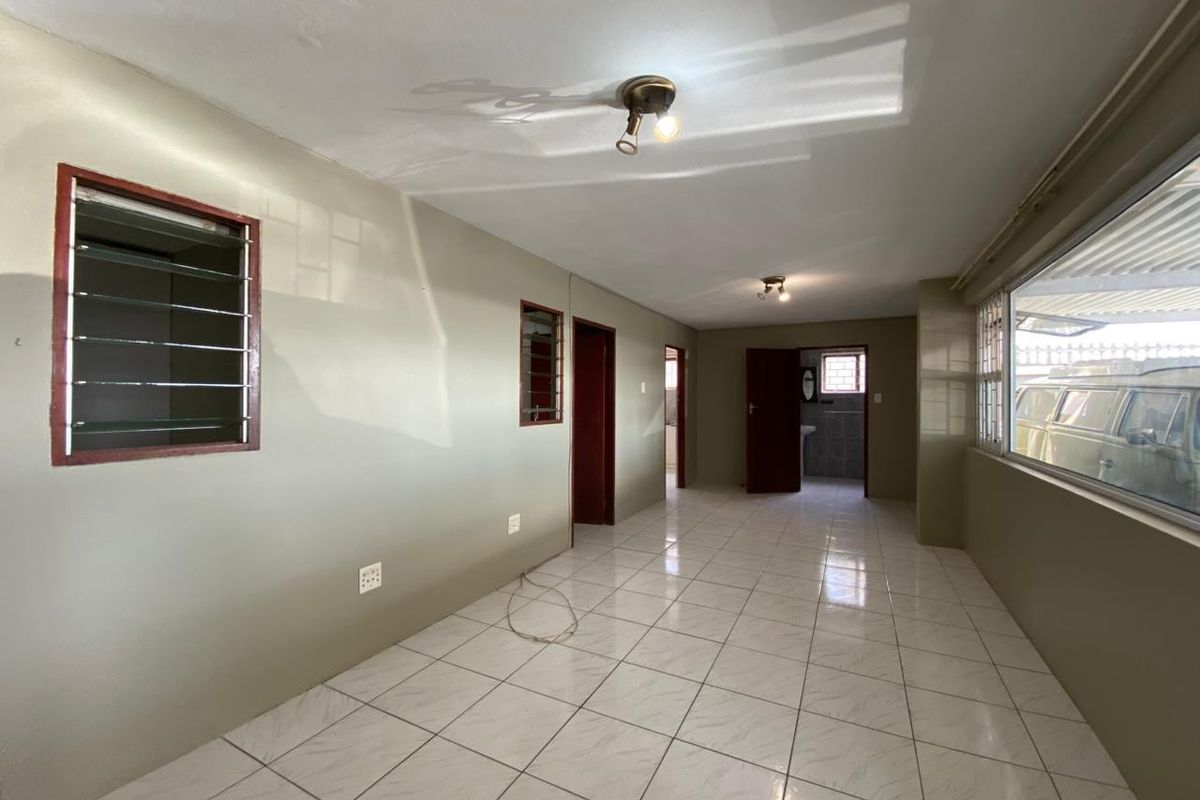 A spacious, empty interior area featuring tiled flooring, multiple doorways, and large windows, offering a versatile layout for living or dining arrangements.