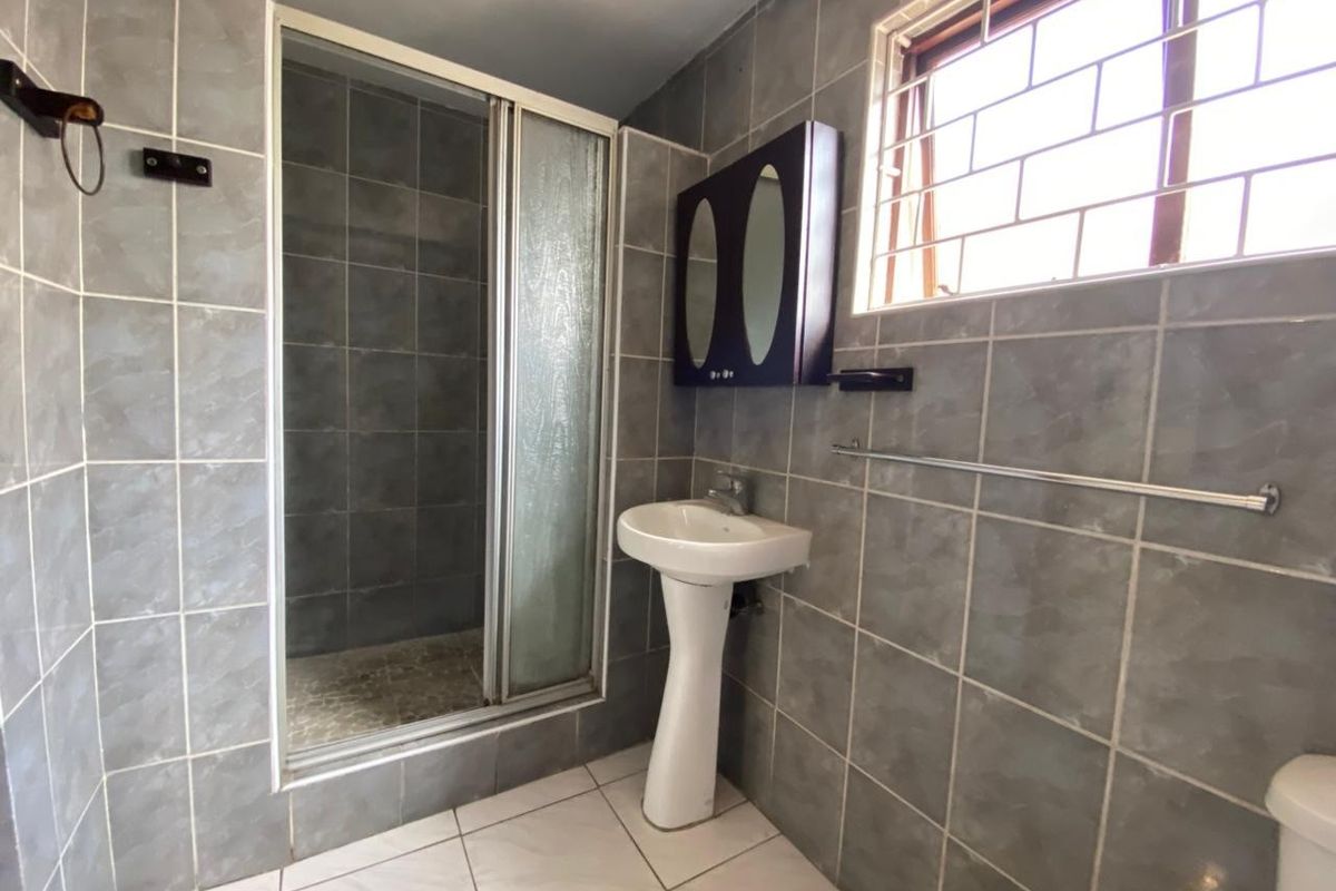 A functional bathroom featuring a glass-enclosed shower, pedestal basin, and wall-mounted medicine cabinet with full-wall tiling.