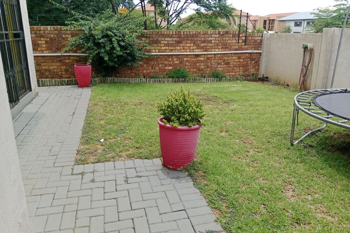 A private rear garden featuring a paved patio area, a small lawn, and a perimeter brick wall with security fencing.