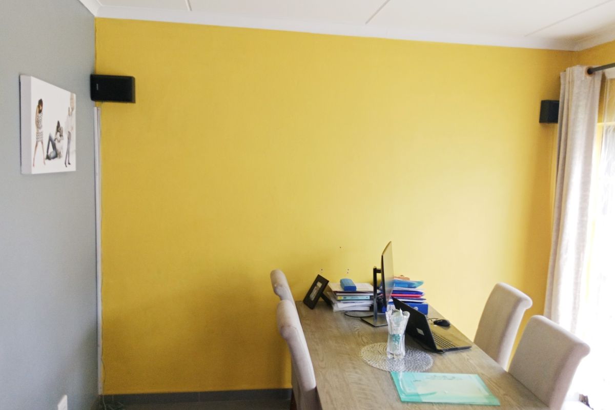 A functional living area featuring yellow accent walls, tiled flooring, and mounted audio speakers.
