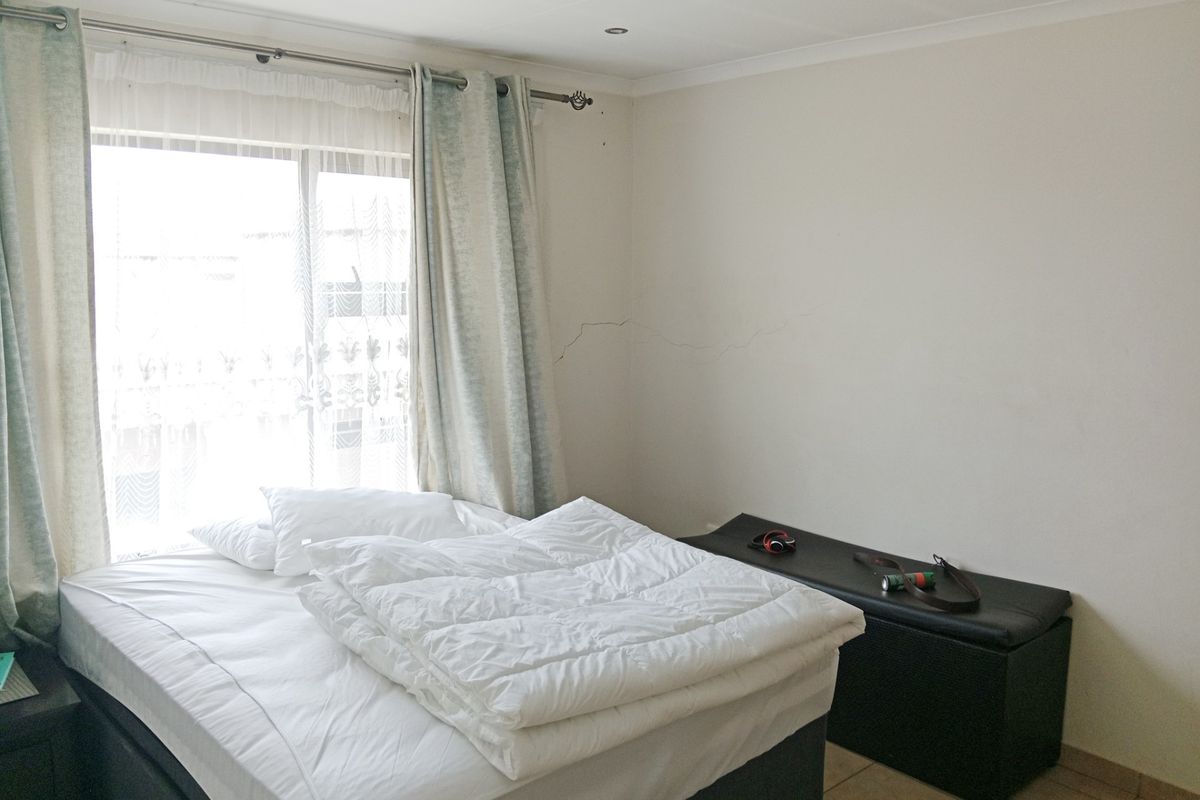 A bedroom featuring tiled flooring and a large window with curtains, showing a visible crack on the wall surface.