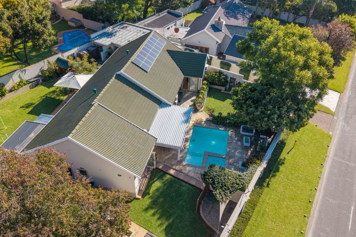 Aerial view of a residential property featuring a tiled roof with solar panels, a swimming pool, a covered patio, and a landscaped garden.