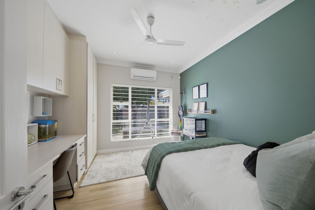 A well-maintained bedroom featuring built-in cabinetry, a study desk, ceiling fan, and split-system air conditioning unit.