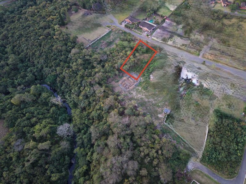 Aerial view of a vacant residential plot situated in a green, established neighborhood with surrounding natural vegetation.