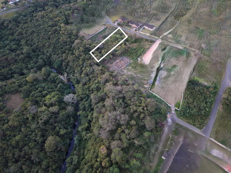 Aerial view of a vacant residential plot situated in a natural, wooded area with nearby road access.