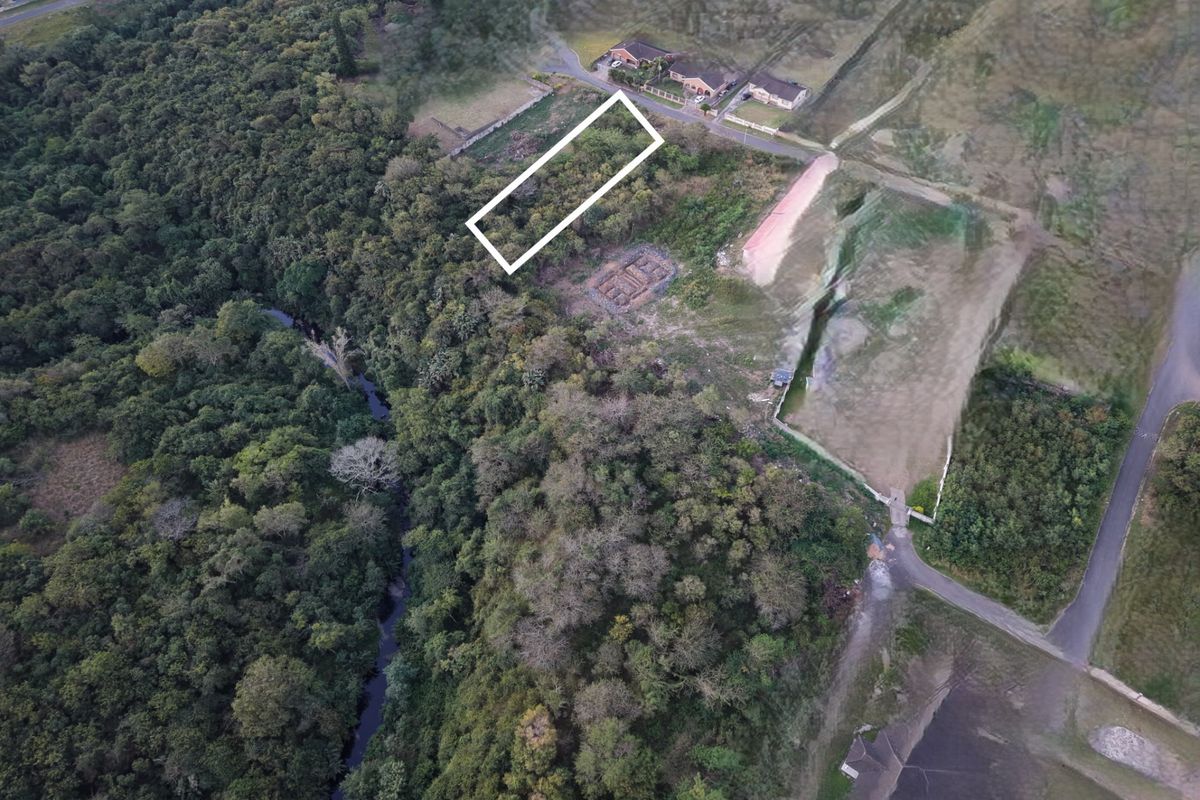 Aerial view of a vacant residential plot situated in a natural, wooded area with nearby road access.
