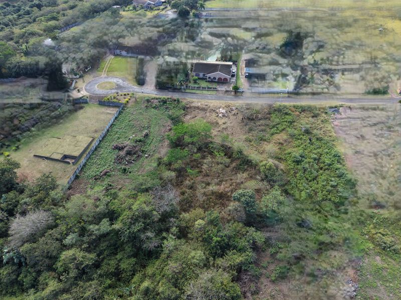 An aerial view of a vacant residential plot featuring natural vegetation and perimeter fencing, situated in a quiet neighborhood setting.