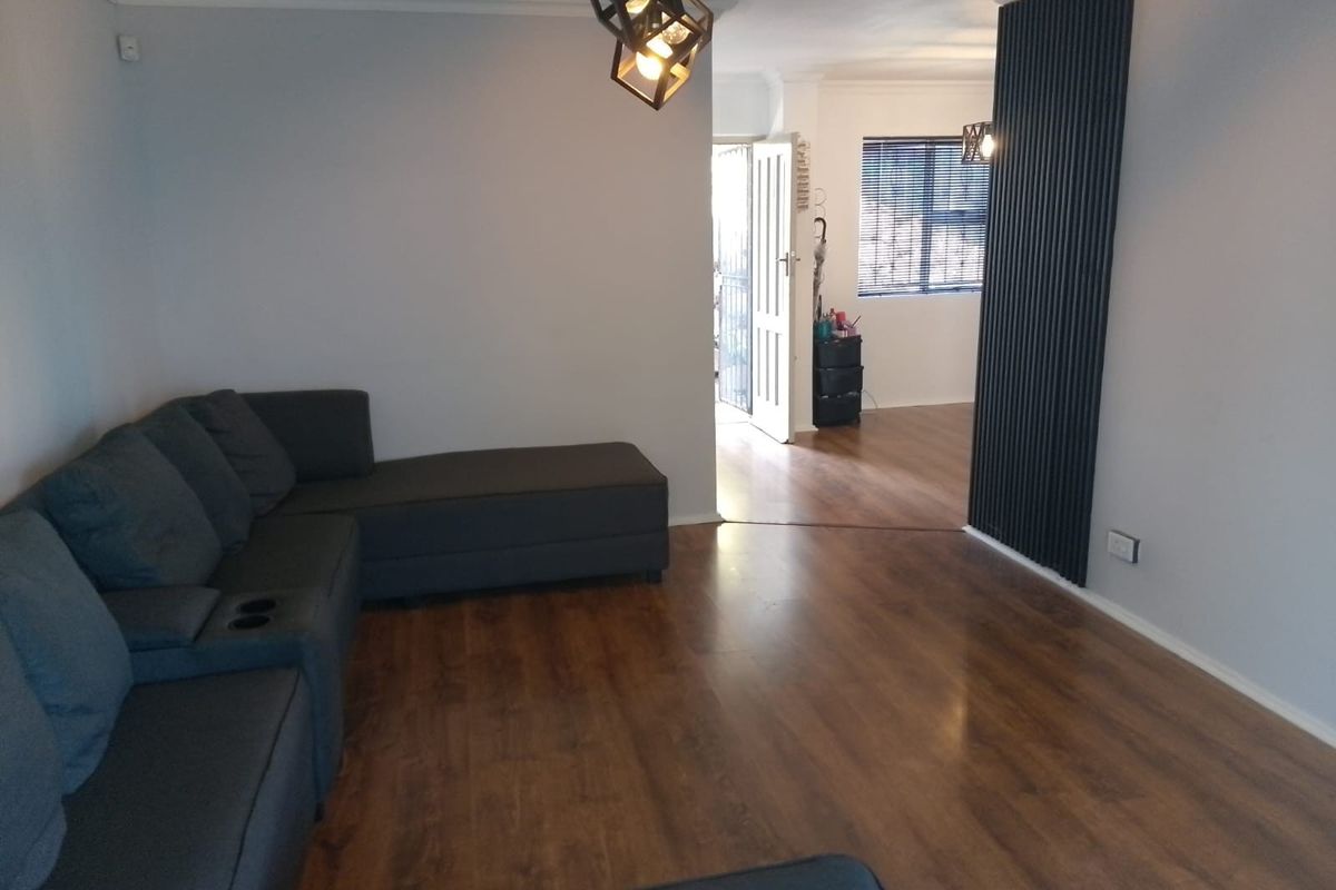 A spacious living area featuring wood-look laminate flooring, a decorative vertical slat feature wall, and modern geometric pendant lighting.