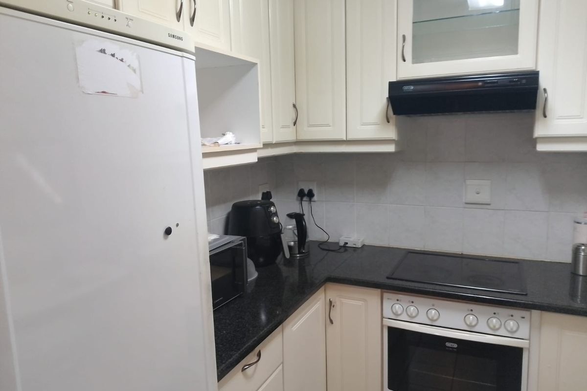 A functional kitchen featuring cream-colored cabinetry, dark granite countertops, a built-in oven, and a black extractor fan.