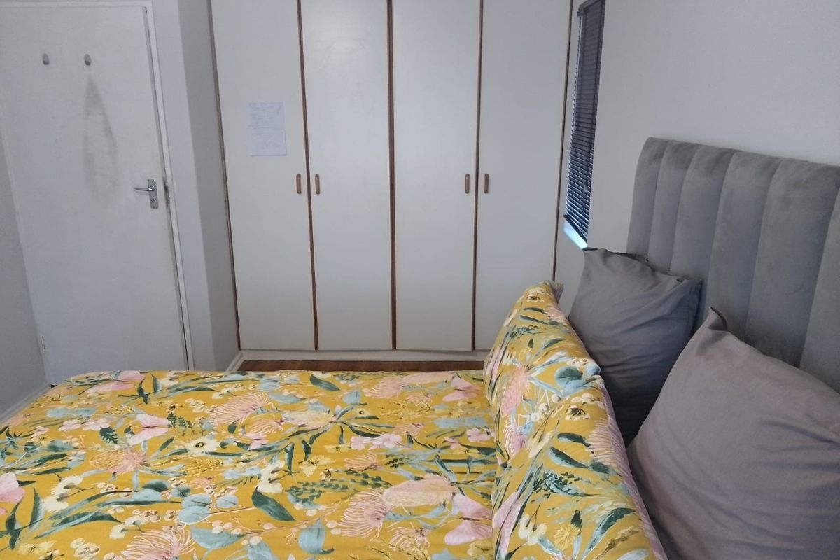 A bedroom featuring built-in wardrobes with white cabinetry and a window fitted with a venetian blind.