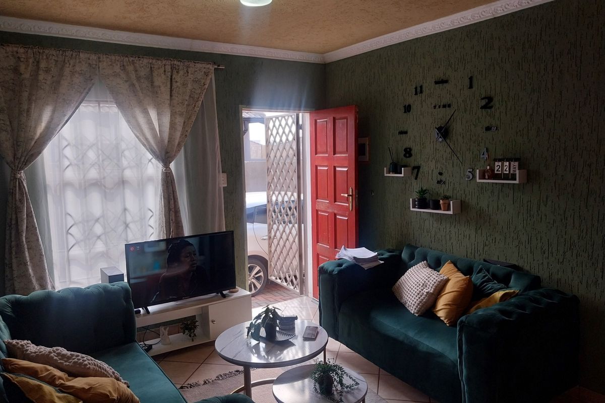 A cozy living room featuring textured green walls, tiled flooring, and direct access to the exterior through a security gate.