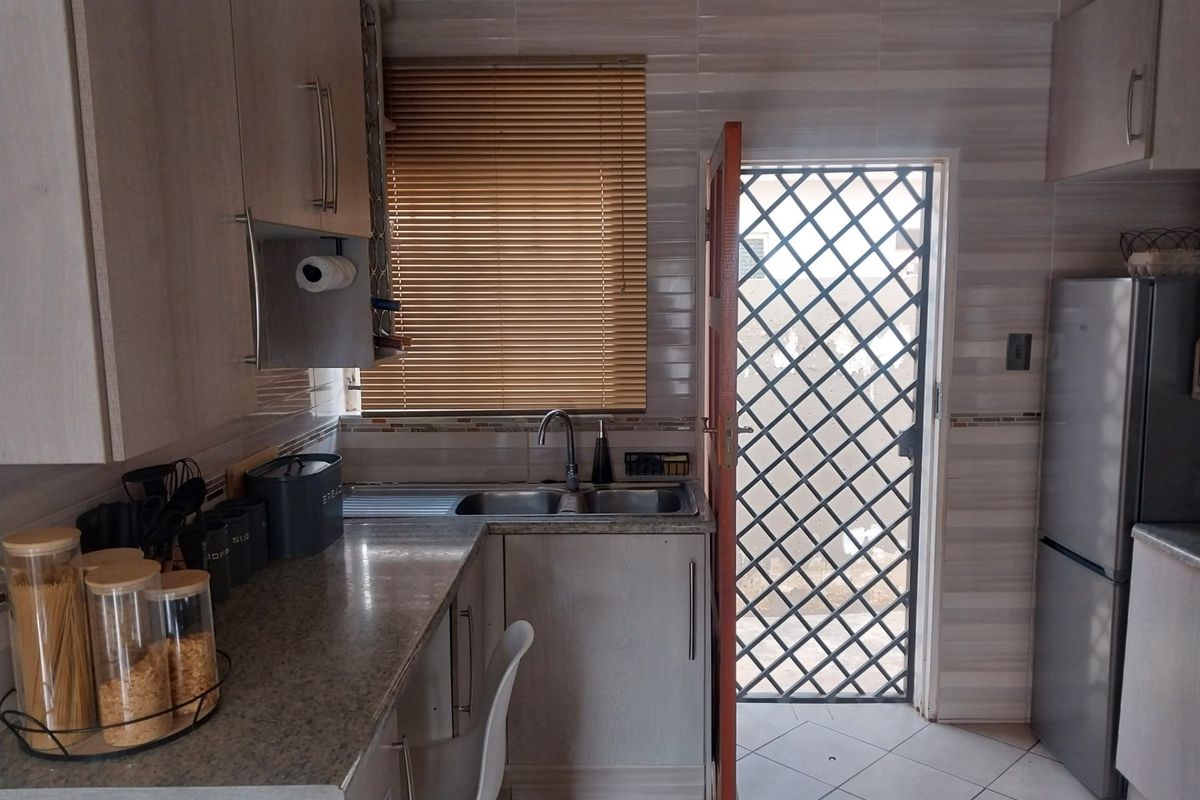 A functional kitchen featuring light-toned cabinetry, granite-look countertops, a double-basin sink, and a security gate leading to the exterior.