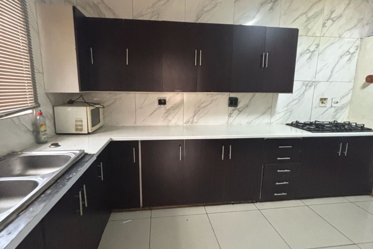 A functional kitchen featuring dark cabinetry, white marble-look wall tiles, a double-basin sink, and a built-in gas hob.