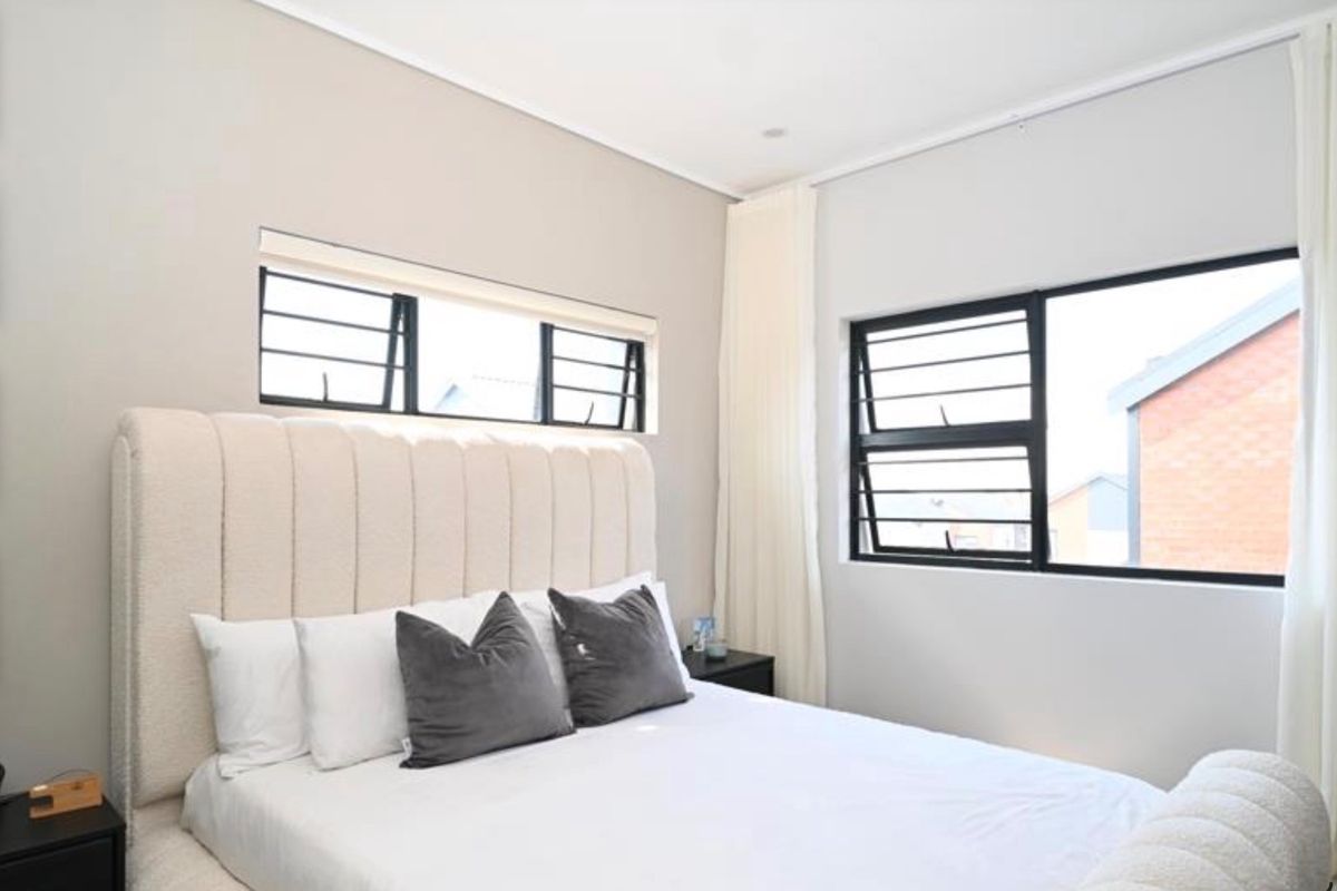 A bright and modern bedroom featuring neutral walls, large windows with security bars, and clean architectural finishes.