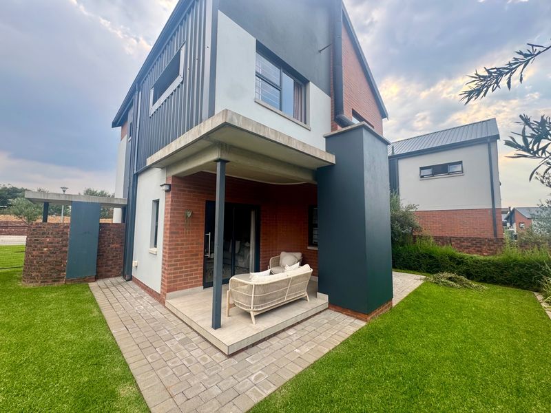 Rear view of a modern townhouse featuring a covered patio, brick and metal cladding exterior, and a well-maintained garden with paved pathways.