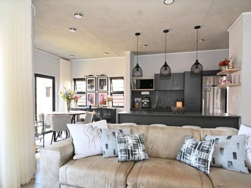Modern open-plan living area featuring a contemporary kitchen with dark cabinetry, a central island, and an exposed concrete ceiling, seamlessly flowing into the dining space.