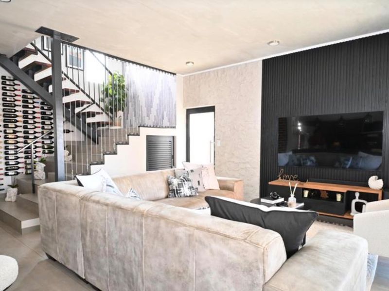 Modern living room featuring a striking open staircase with integrated wine storage and a textured black feature wall.