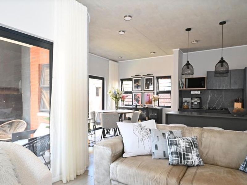 Modern open-plan living area featuring a sleek kitchen with island, recessed lighting, and seamless flow to an outdoor patio through large sliding glass doors.