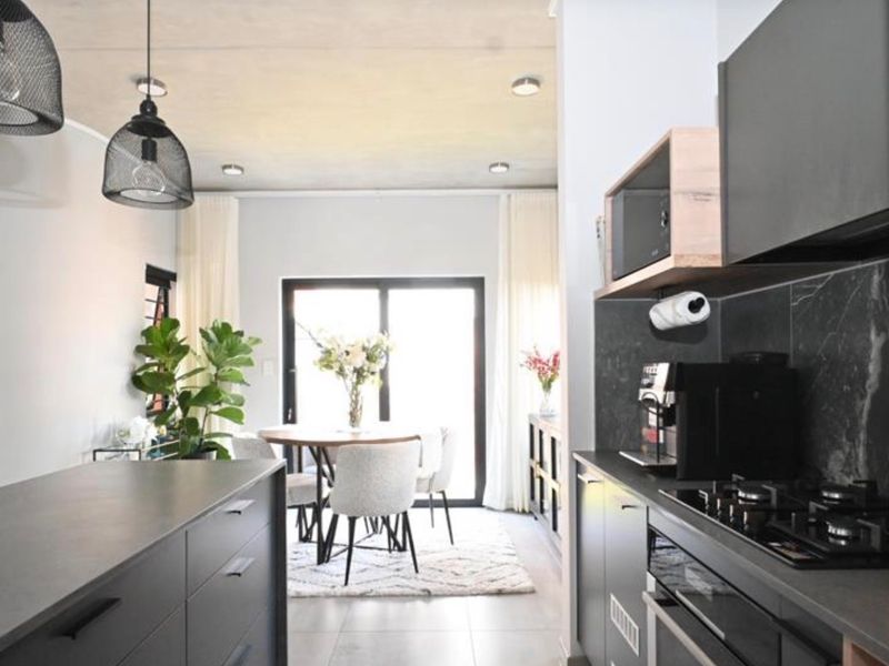 Modern open-plan kitchen and dining area featuring sleek dark cabinetry, stone countertops, integrated appliances, and sliding doors leading to the outdoors.