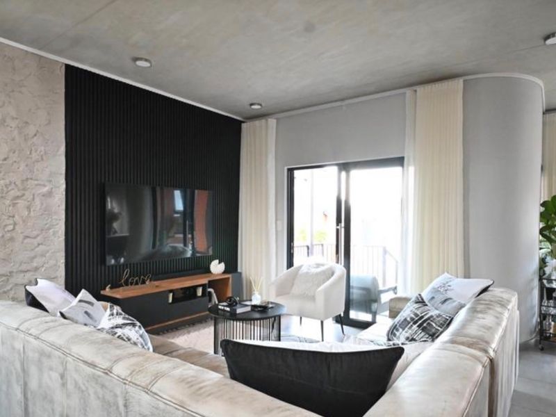 Modern living room featuring a textured feature wall, exposed concrete ceiling, recessed lighting, and large sliding glass doors providing access to the outdoors.