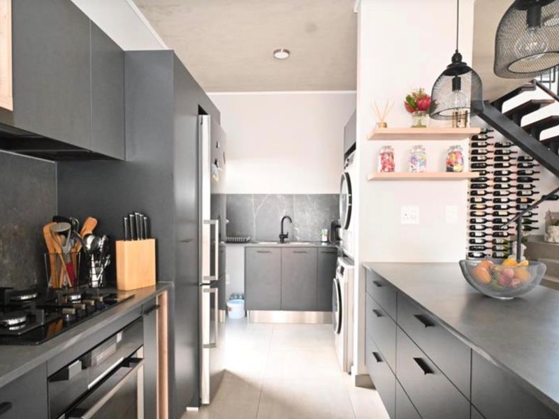 Modern kitchen featuring dark cabinetry, stone countertops, integrated appliances, and a built-in wine rack, adjacent to an open staircase.