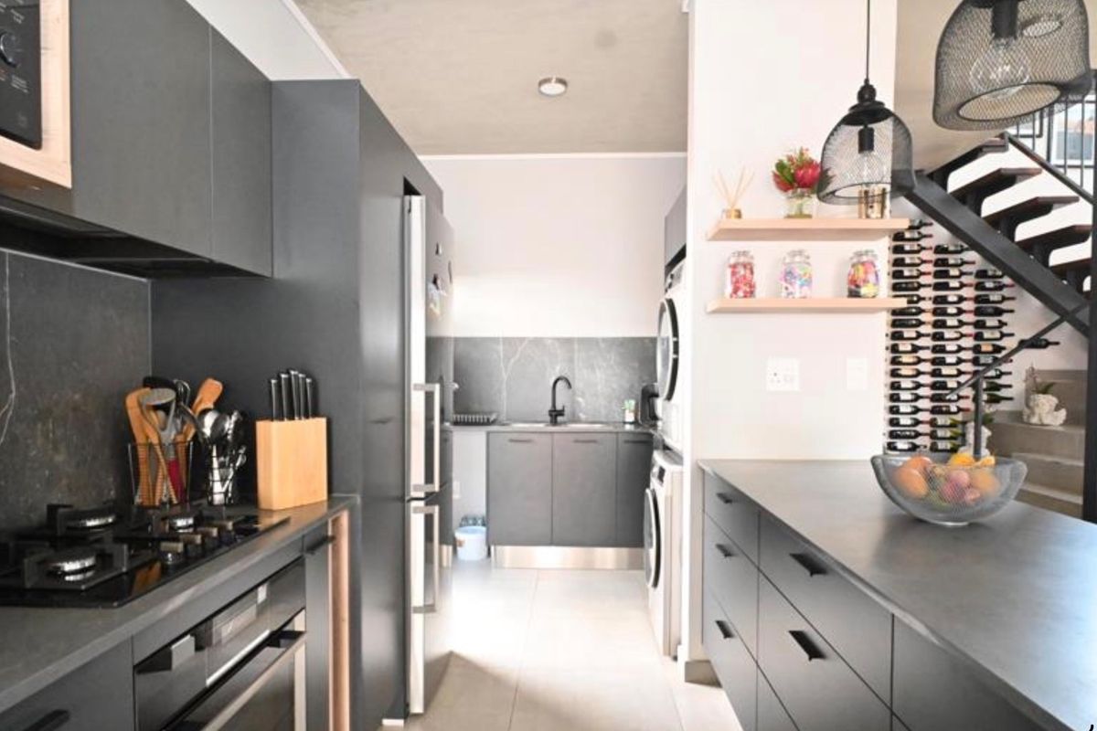 Modern kitchen featuring dark cabinetry, stone countertops, integrated appliances, and a built-in wine rack, adjacent to an open staircase.