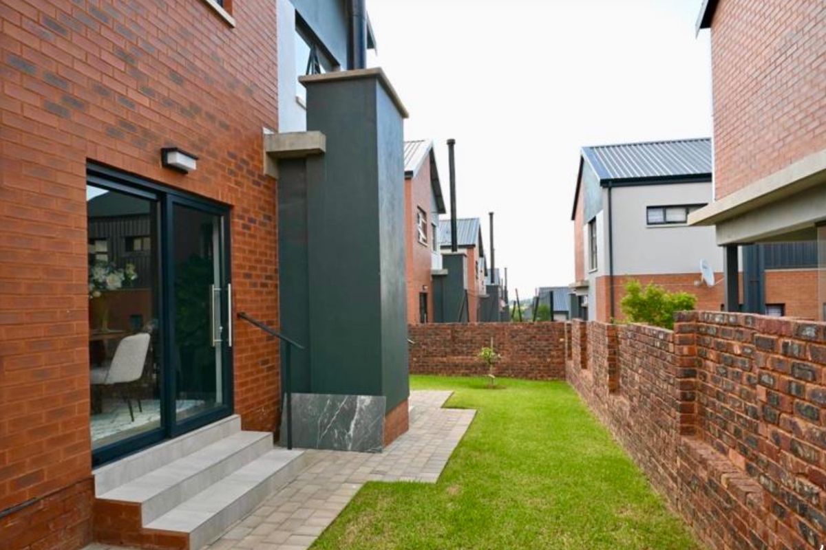 Rear view of a modern townhouse featuring a face brick facade, paved patio area, and a private garden enclosed by a brick boundary wall.