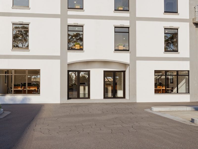 A modern commercial building facade featuring large glass windows, double entrance doors, and a paved driveway area.