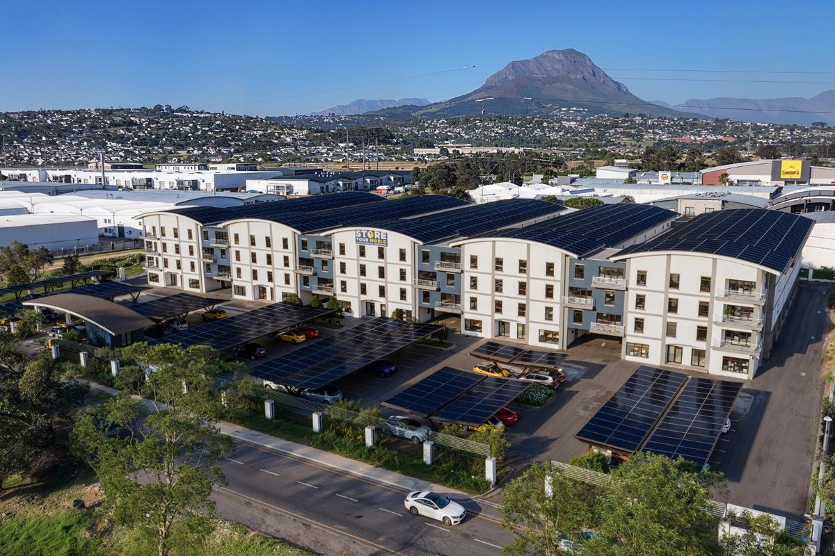 Aerial view of a modern commercial complex featuring extensive rooftop and carport solar panel installations, ample parking, and mountain views.