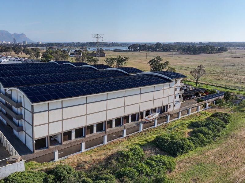 Aerial view of a large commercial warehouse facility featuring an extensive rooftop solar panel installation and secure perimeter fencing.