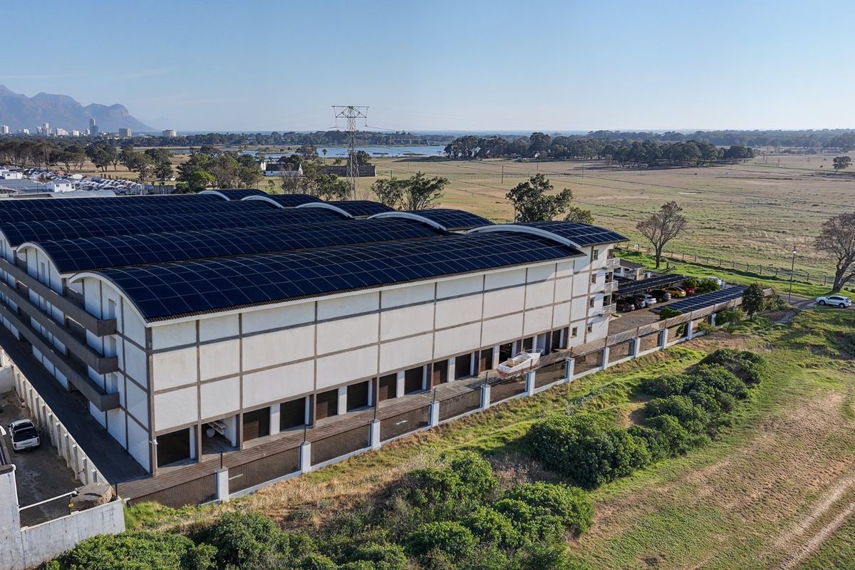 Aerial view of a large commercial warehouse facility featuring an extensive rooftop solar panel installation and secure perimeter fencing.