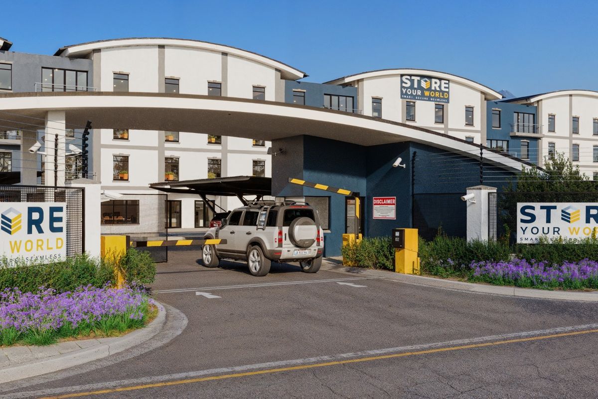 A secure commercial facility entrance featuring a modern arched gate structure, automated boom barrier, and professional signage for Store Your World.