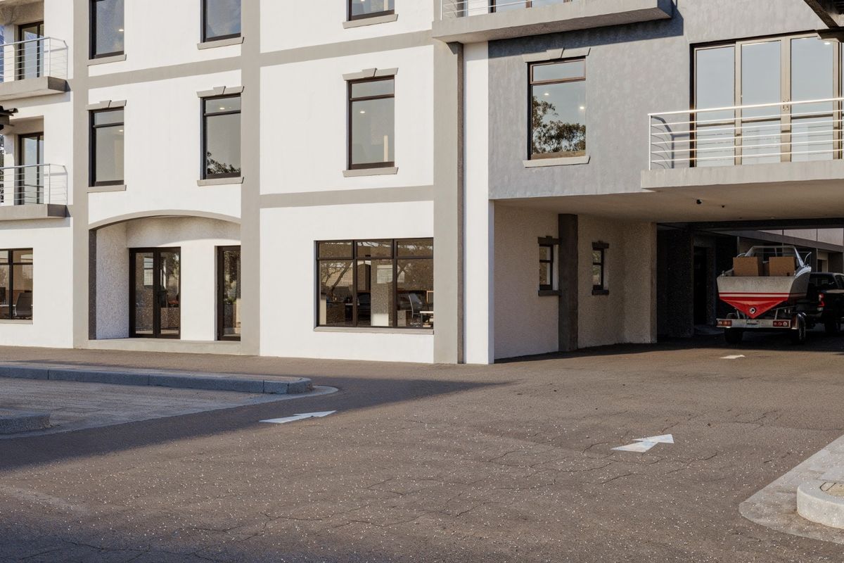 Modern commercial building exterior featuring a paved driveway, covered parking area, and large glass windows with a clean, contemporary facade.