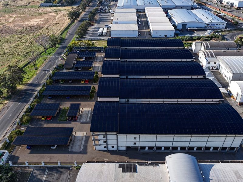 Aerial view of a commercial warehouse facility featuring extensive rooftop solar panel installations and covered parking bays.