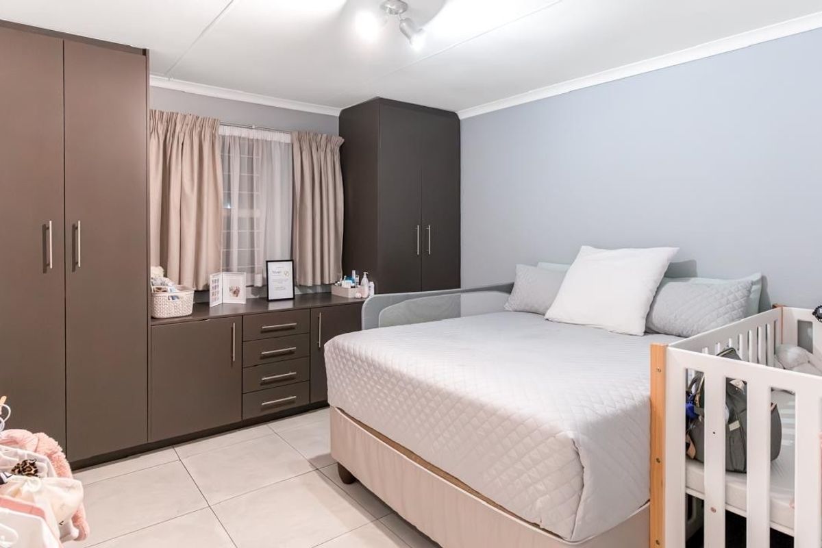 A well-maintained bedroom featuring neutral wall tones, tiled flooring, and extensive built-in cupboard storage.