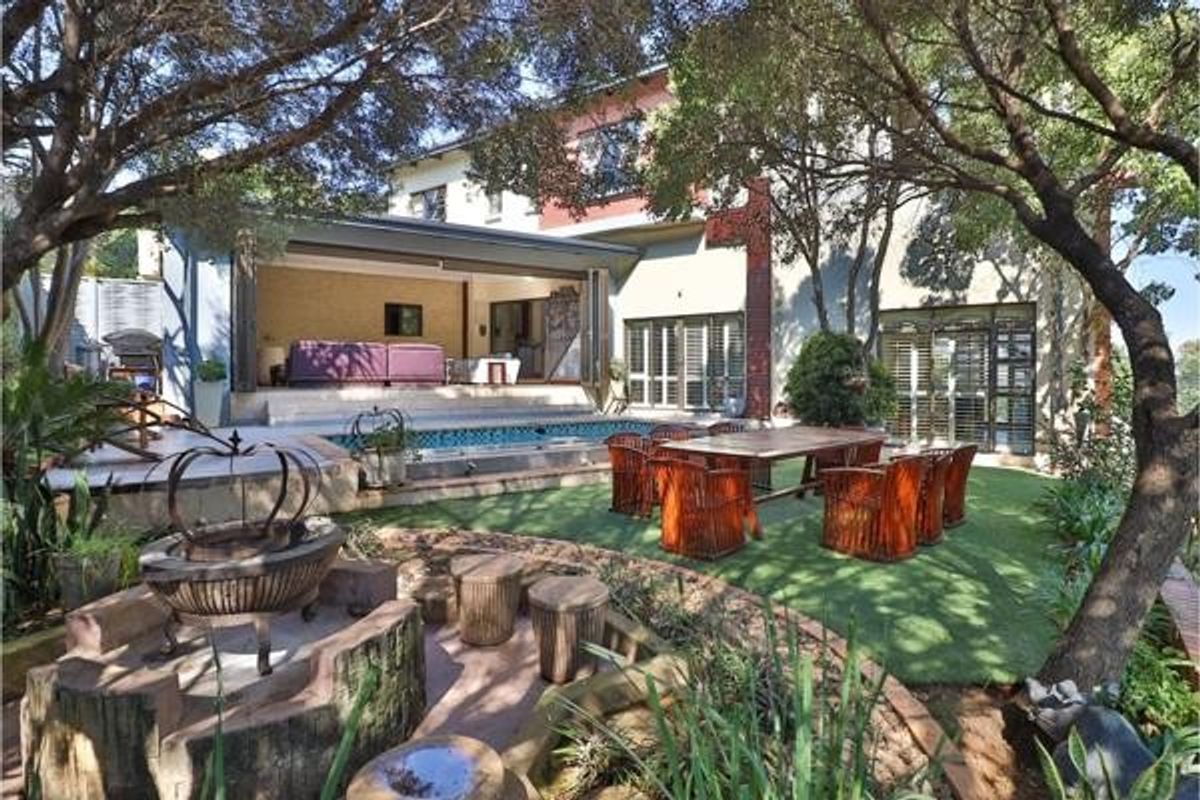 Rear exterior view featuring a swimming pool, artificial lawn, stone fire pit, and seamless indoor-outdoor flow through large bi-fold doors.