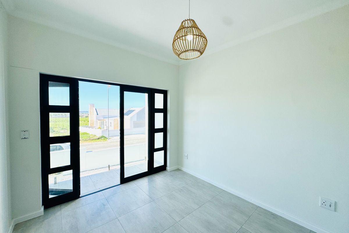 A bright, empty room featuring large black-framed sliding glass doors that open to an outdoor area, complemented by neutral floor tiling.