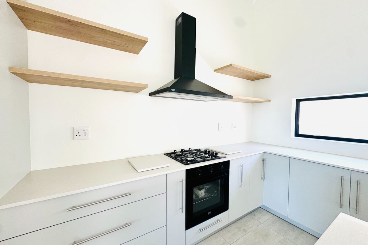 Modern kitchen featuring light grey cabinetry, stone countertops, built-in gas hob, electric oven, black extractor fan, and floating timber shelving.