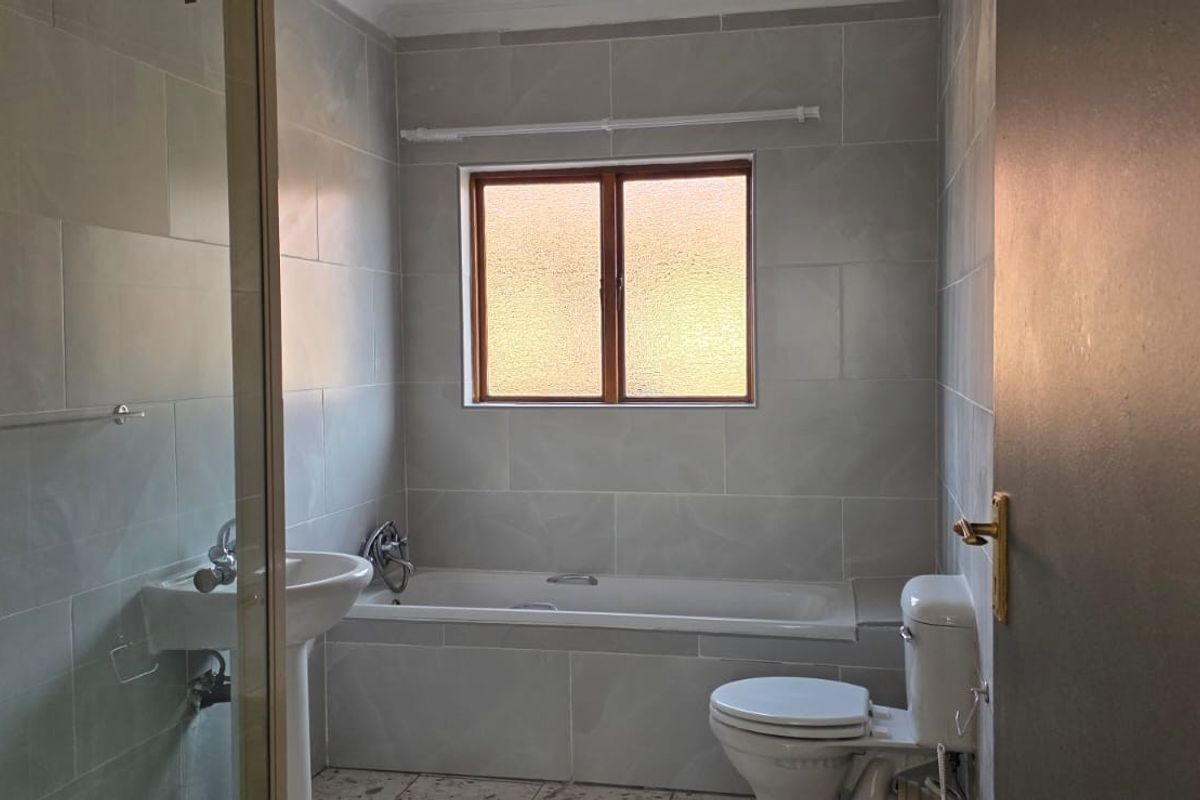 A functional bathroom featuring a pedestal basin, a built-in bathtub, and a toilet, finished with neutral wall tiling.