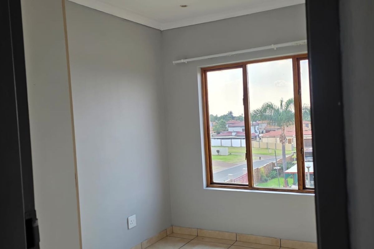 A bright, empty bedroom featuring neutral grey walls, tiled flooring, and a large window with wooden frames offering a view of the neighborhood.