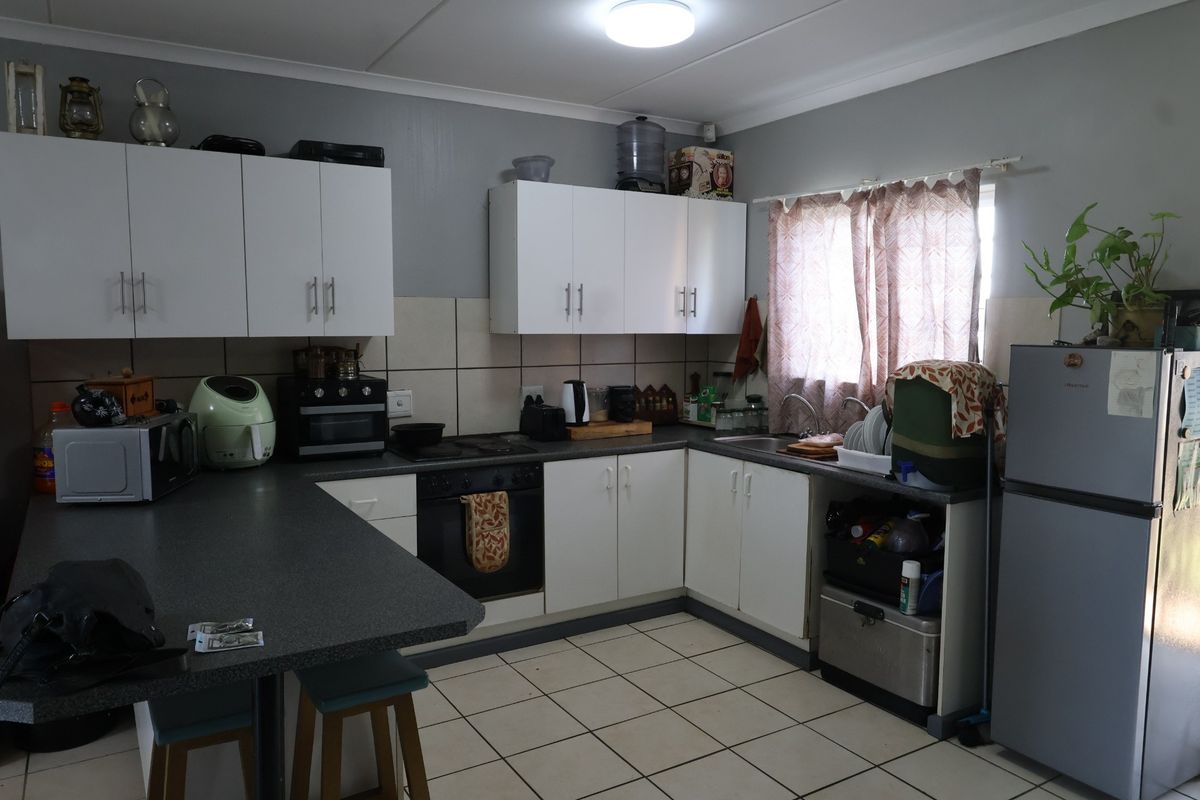 Functional kitchen featuring white cabinetry, dark laminate countertops, tiled backsplash, and ceramic floor tiles, offering a practical layout for daily meal preparation.