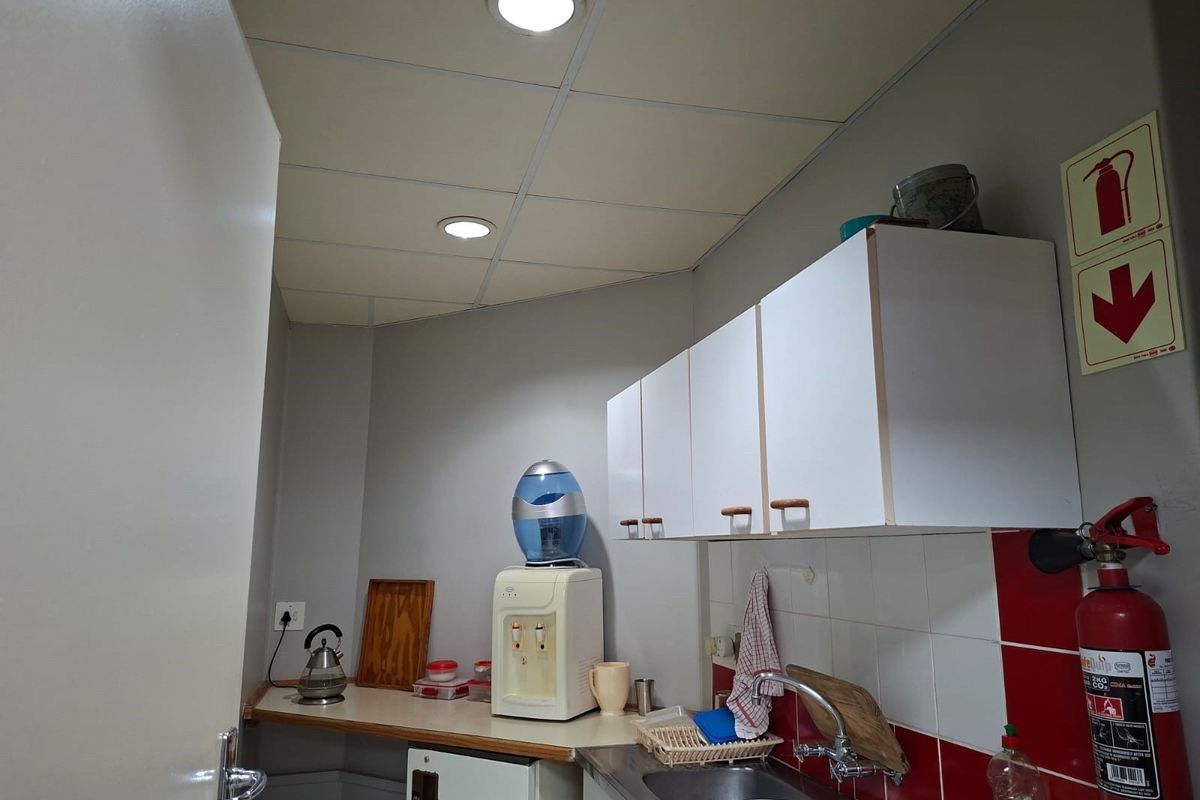 A functional office kitchenette featuring built-in cabinetry, a stainless steel sink, and a tiled splashback, equipped with essential fire safety equipment.